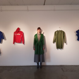 MLF Tarza & Jane latex fashion expo at Galerie vorn und oben, Mona in green coat in front of red top and sweatshirt dress